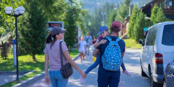Parents walking with their daughter in a picturesque mountain village, enjoying a sunny day outdoors.