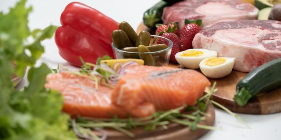 A vibrant assortment of fresh salmon, eggs, vegetables, and fruits arranged on a wooden platter.
