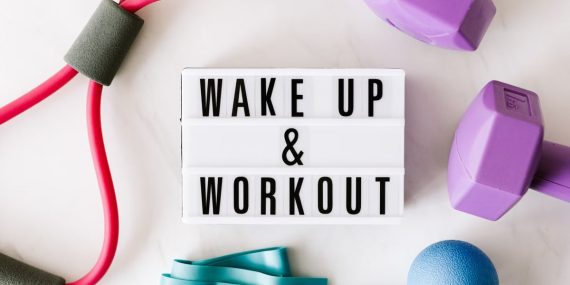 Top view closeup composition of wake up and workout inscription on light box surface among expanders and dumbbells and massage ball on white background